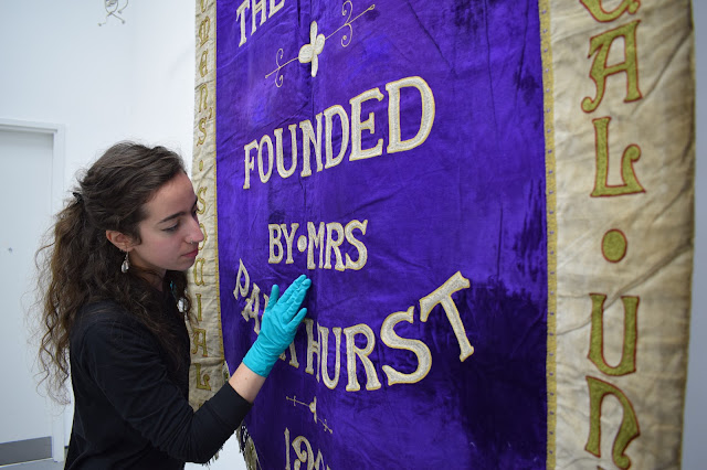 Female curator checking the purple suffrage banner with gloved hand
