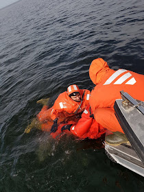 Yksi henkilö veneessä auttaa kahta pelastautumispukuista veneeseen