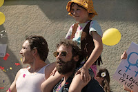 young girl sits on her father’s shoulders at a Pride parade