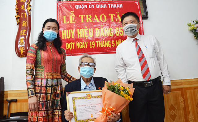 Đồng chí Triệu Lệ Khánh, Phó Bí thư Thường trực Quận ủy cùng đồng chí Nguyễn Văn Quý, Bí thư Đảng ủy Phường 26 trao Huy hiệu, tặng hoa chúc mừng đảng viên Bùi Văn Hoành (65 tuổi Đảng). (Ảnh MD)