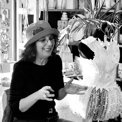 smiling woman wearing hat motioning toward handmade paper dress