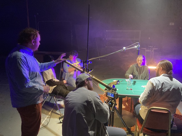 Movie director on set of a filming, with actors around a poker table