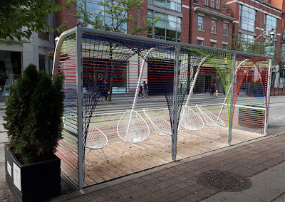 A seating area created by stringing colourful ropes around a steel frames. Chairs are round and strung with white cords.