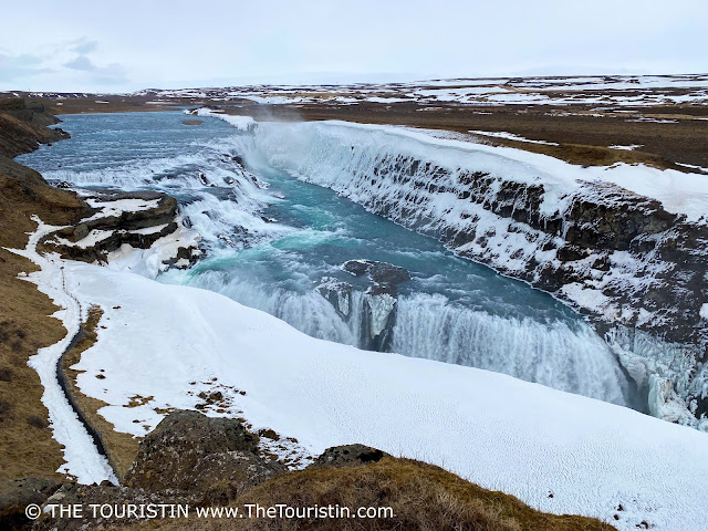 A wintry snowy landscape where blue-green coloured water cascades down a large waterfall.