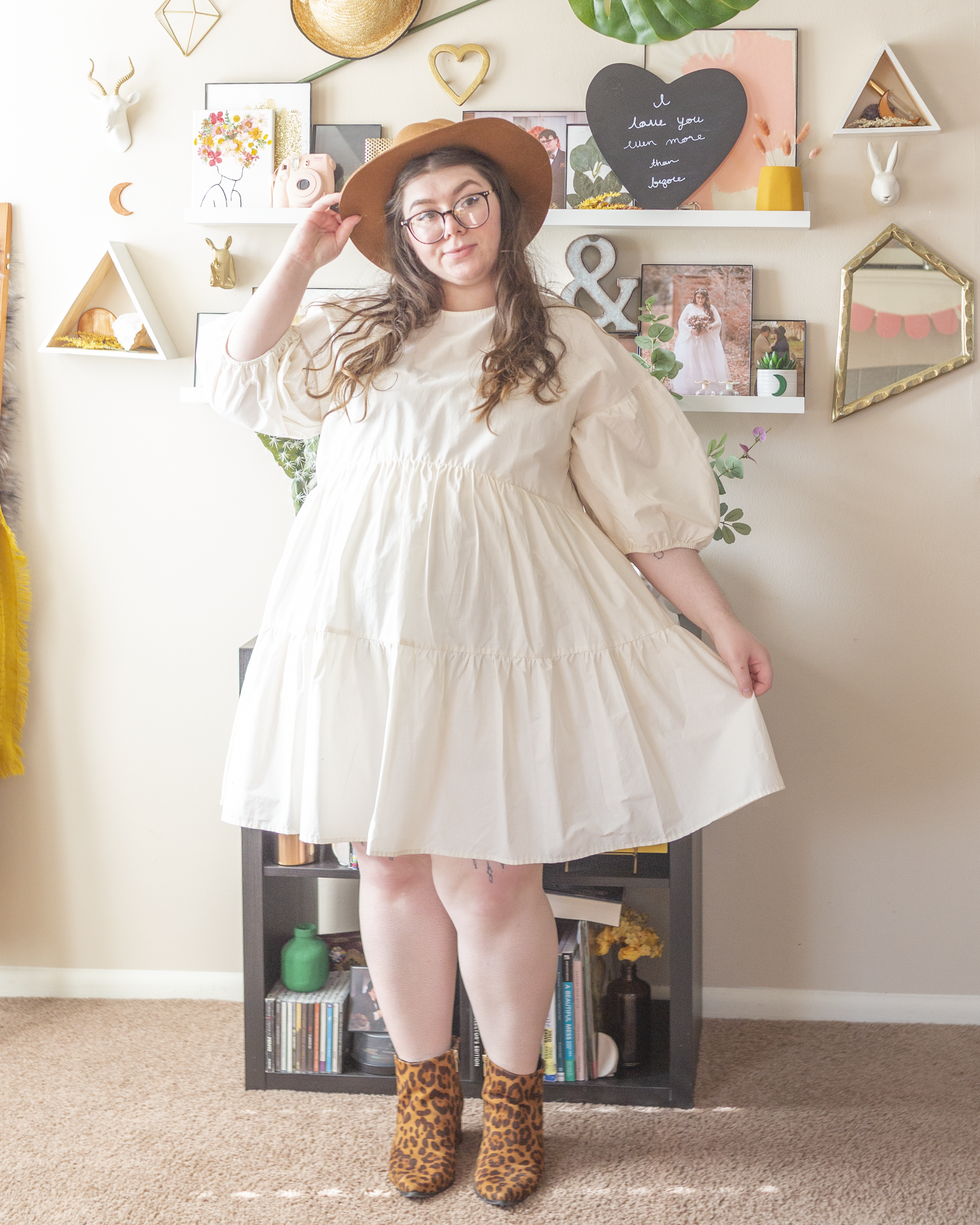 An outfit consisting of a camel brown panama hat, a white 3/4 sleeve tiered ruffle midi dress with puff sleeves, and brown leopard print ankle boot.