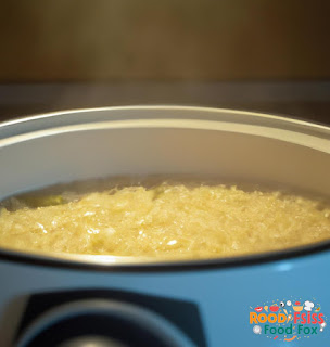 This image shows a pot of the Greek Lemon Rice Soup cooking on the stove. The steam rising from the pot creates an inviting and comforting atmosphere. The soup looks creamy and flavorful, with grains of rice visible throughout.