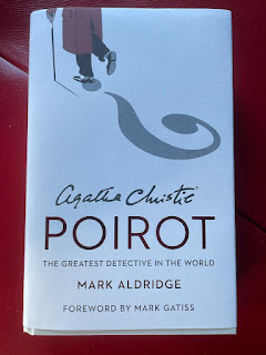 There is a book cover showing the character of Hercule Poirot's walking away, with his shadow forming the shape of a question mark. The cover has the following information -  Agatha Christie Poirot, the greatest detective in the world,  by Mark Aldridge. The foreword is by Mark Gatiss.