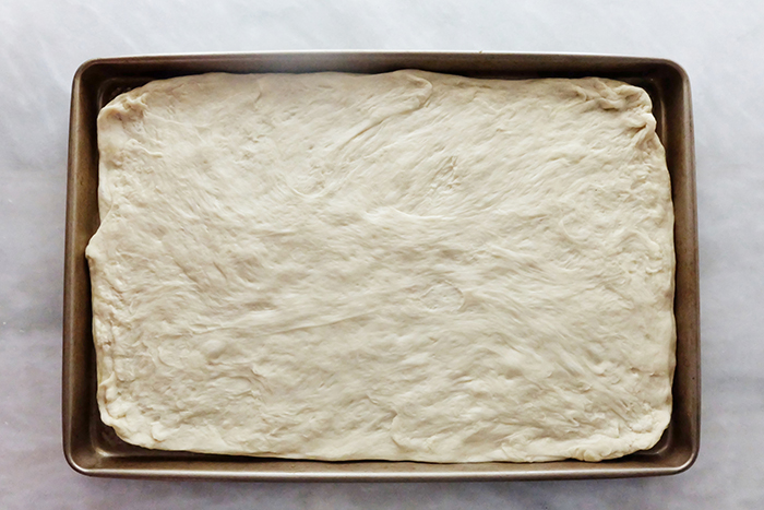 stretching pizza dough in rimmed baking sheet