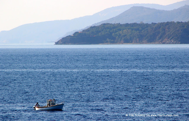 A tiny fishing boat in the sea with a mountain range in the distance.