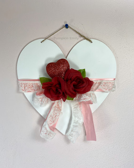 A heart wall hanging with roses, a glitter heart, leaves, lace, and ribbon.