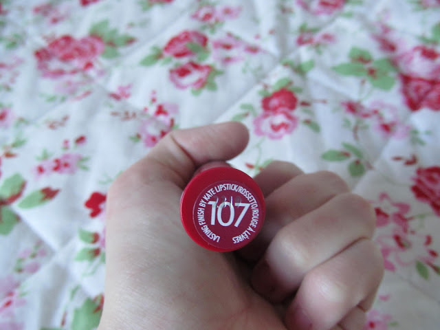 white hand holding red lipstick bottom up to show '107' burgundy sticker on bottom