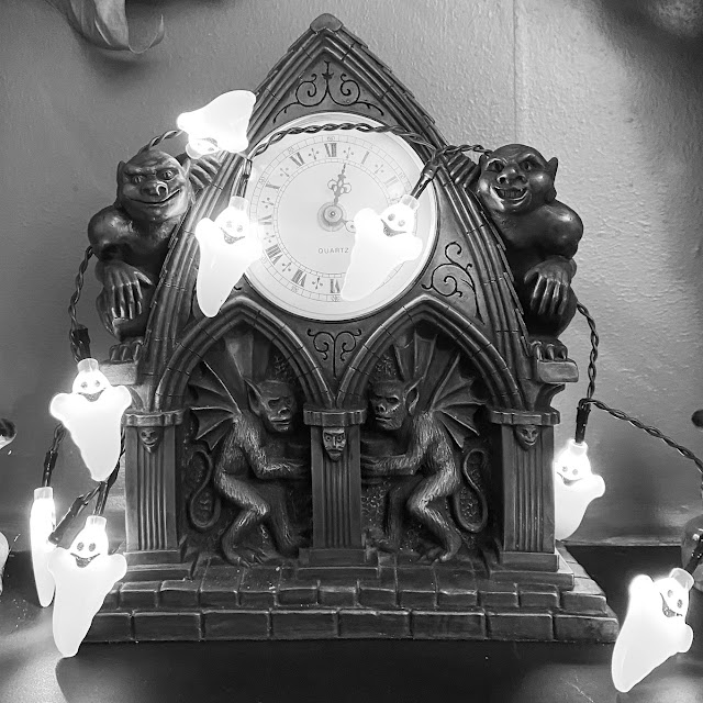 A string of little ghost-shaped lights draped over a clock shaped like a gothic arch covered in gargoyles.