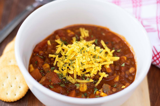 The Perfect Chili, finished, in a white bowl, topped with cheese, and crackers on the side.