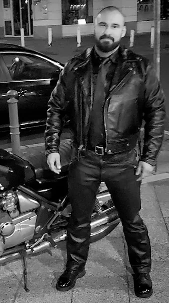 Black and white full view of a tough man wearing all black leather biker gear pumping gas