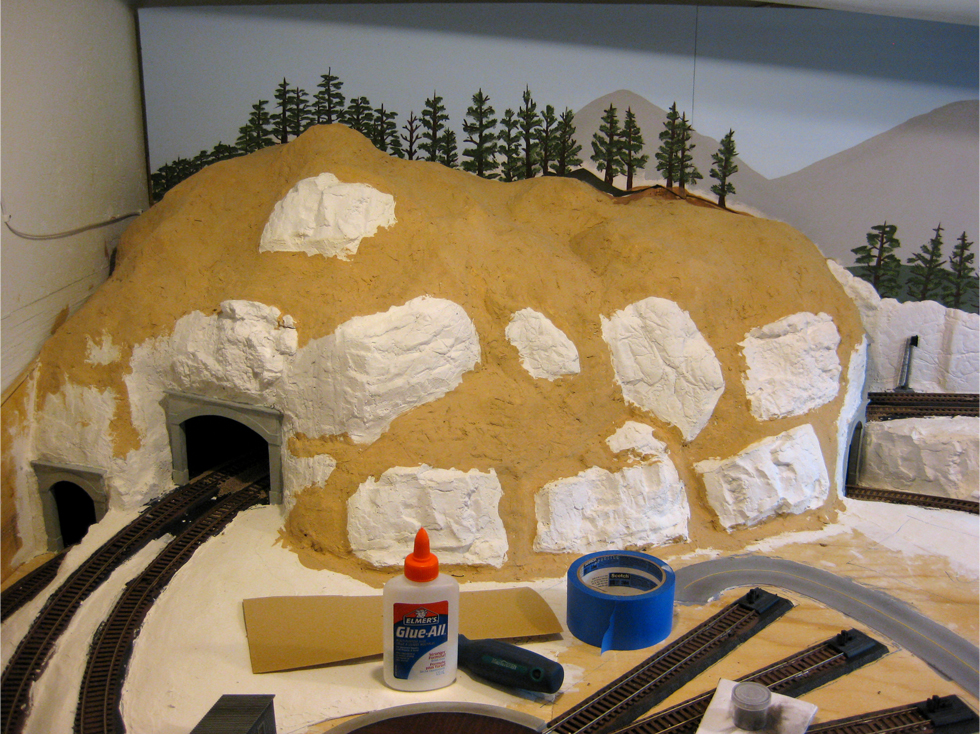 Hard shell plaster mountain terrain being painted with tan colour acrylic paint