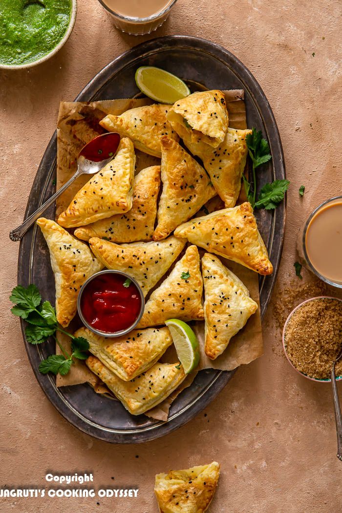 Air fryer Punjabi samosa puffs served in a oval tray with tomato ketchup, masala chai and green chutney next to it.