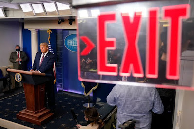 Donald Trump at podium with Exit sign in foreground.