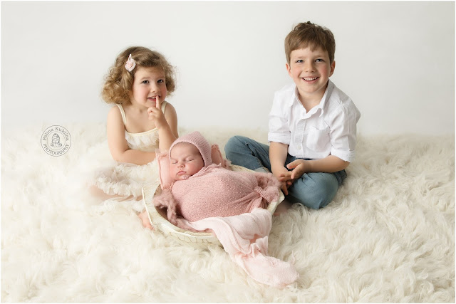 Sleeping baby girl in pink blanket with brother and sister next to her