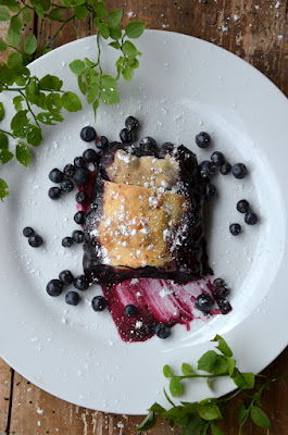 Fertig gebackener Waldheidelbeer-Strudel auf einem weißen Teller angerichtet, daneben liegen Waldheidelbeer-Blätter.