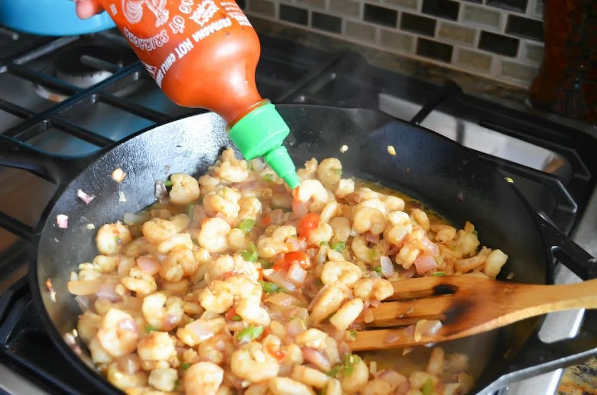 Siraracha Hot Sauce being added to shrimp in cast iron pan.