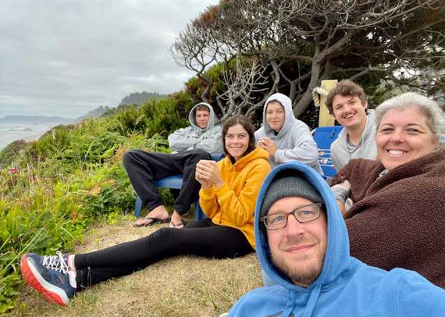 The six. You are sitting on the ground drinking a cup of hot chocolate. The rest of us are sitting in chairs behind you. We are in the backyard overlooking the ocean.
