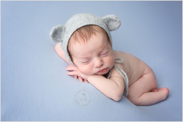 Newborn baby boy is posed on a blue blanket with his head on his hands. 
