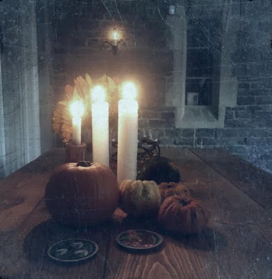 Grey filtered image of a wooden table with multiple pumpkins and lit candles
