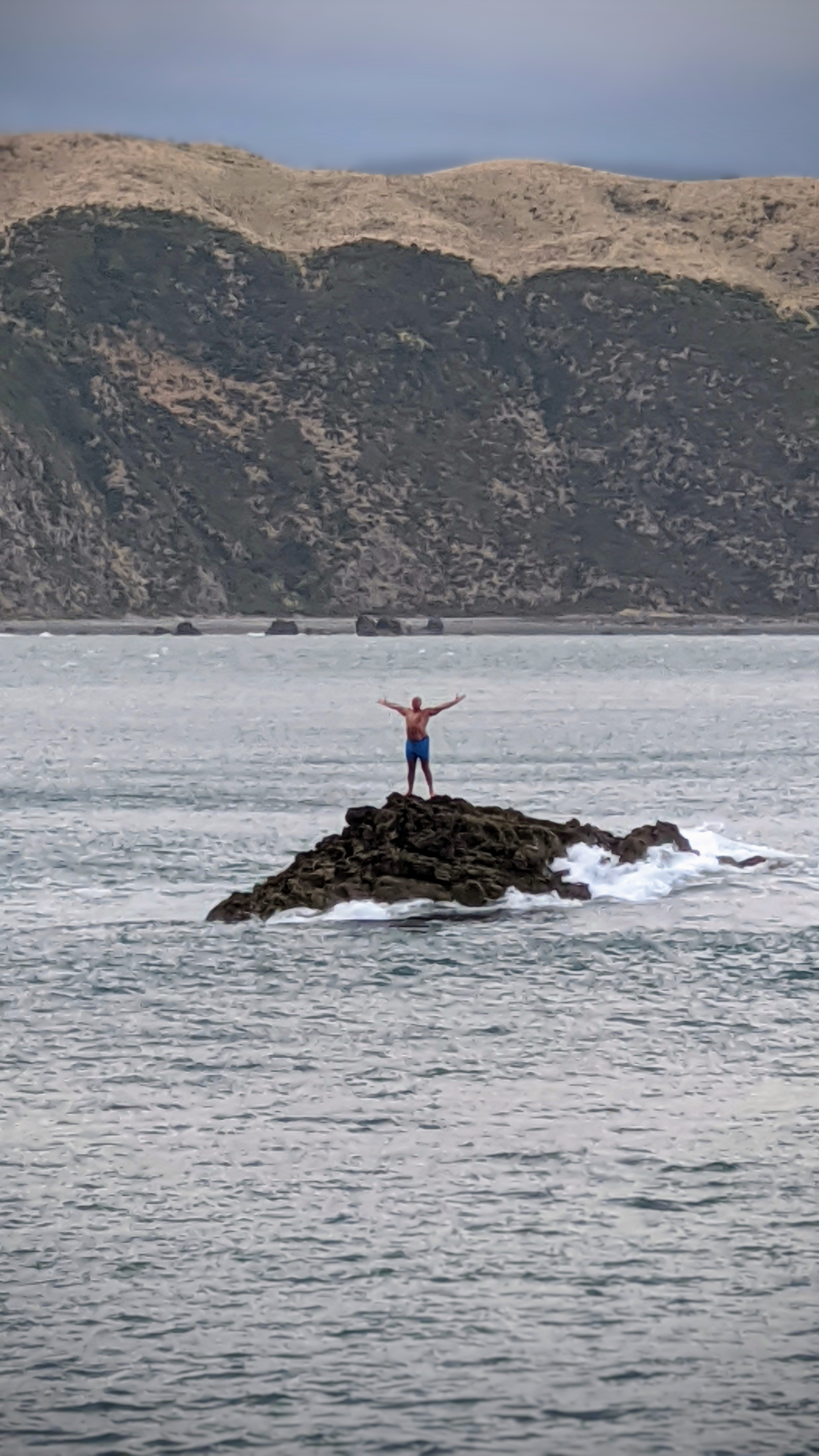 Swimmer stands on Breaker Bay rock with arms outstretched in triumph