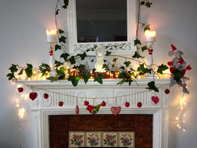 White victorian mantlepiece with ivy, candles and fairy lights christmas decorations and some red decorations to add colour.hts