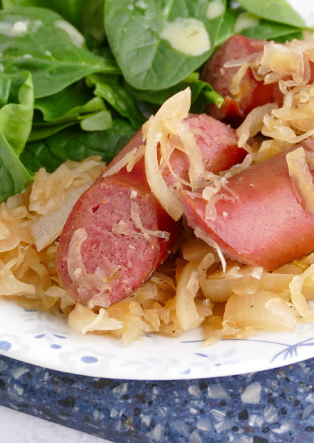 Kielbasa and Sauerkraut on a plate with spinach on the side.
