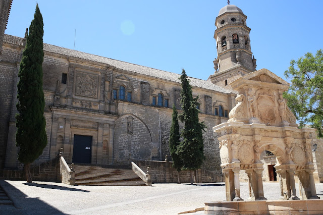 Plaza medieval con una fuente de piedra y una catedral al fondo.