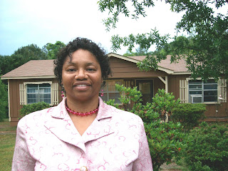 African American student with rose pink suit matching accessories,freckles in face with a beautiful smile standing in her front yard by a green hedge bush