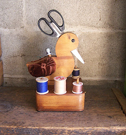 wooden bird holding scissors and thimble, with spools of thread at the base