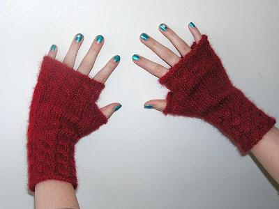 two hands with blue nailpolish and red fingerless gloves on a white wall