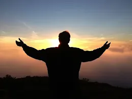 A man standing in front of sunset with arms wide open