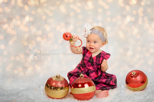 beautiful toddler girl sitting on white rug with white background with christmas lights