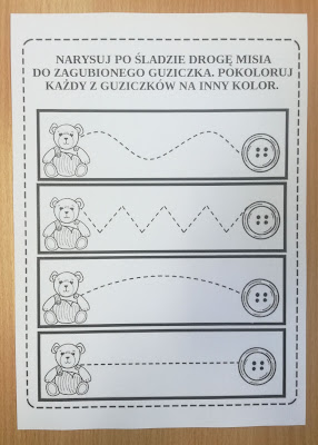 Brązowe tło biała kartka z zadaniem dla dzieci Narysuj po śladzie drogę misia do zagubionego guziczka pokoloruj każdy z guziczków na inny kolor