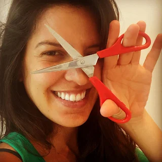 smiling woman holds pair of scissors with opened blades in front of face