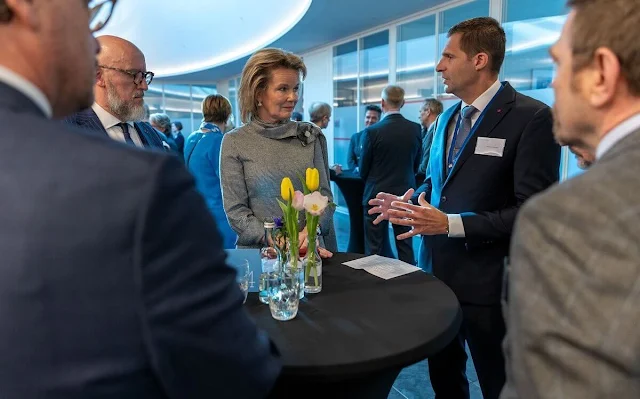 Queen Mathilde wears a black and white checked dress, with a wine-red cape coat by Natan. Diamond parrots brooch