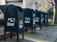 5 U.S. Postal mailboxes aligned in a row on a drive-by sidewalk