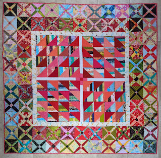 Medallion scrap quilt has The Square Deal block in the center surrounded by a narrow, white inner border and an outer border of two rows of lattice blocks in shades of red, pink, blue, and green