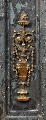 Dekoracja reliefowa oparta na motywie geometrycznego kandelabru z elementami girland kwiatowych. Całość zwieńczona płomieniem.