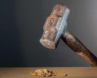 Image shows a heavy hammer held over a crushed nut.