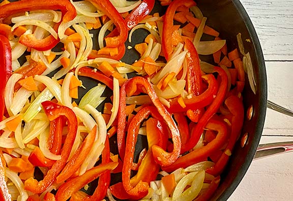 Peppers, carrots and onions frying in a pan.