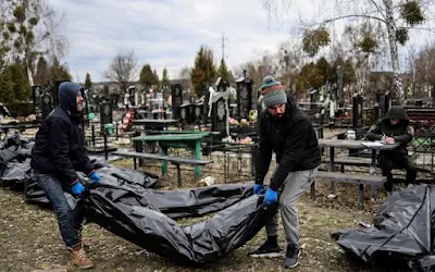 Trabalhadores carregam um saco de cadáveres para que possa ser identificado por autoridades forenses, em um cemitério em Bucha, perto de Kiev. Foto: AFP