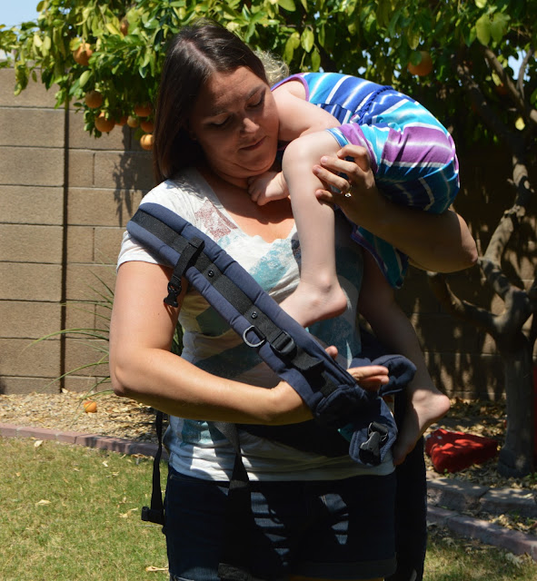 Momma is guiding her baby's leg into the right side of the carrier