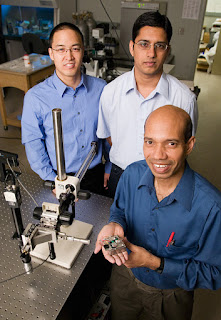 Taher Saif, a professor of mechanical science and engineering, holds a piezo actuated stage for nanoscale material studies in scanning electron microscopes. Graduate students Jong Han, left, and Jagannathan Rajagopalan explored aluminum films and gold films. Photo by L. Brian Stauffer