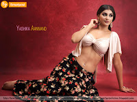 yashika aannand sitting on floor with bare feet, navel shoe, white bra and top with black floral skirt, red abstract background