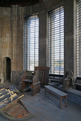 Discarded woodwork including some pulpit steps, in a room lined with tall windows.