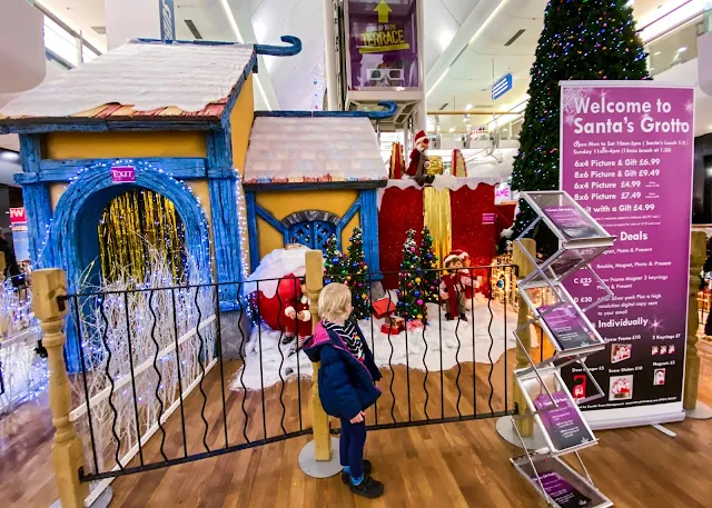 A girl looking at the Harvey Centre Santa's Christmas Grotto next to the price list